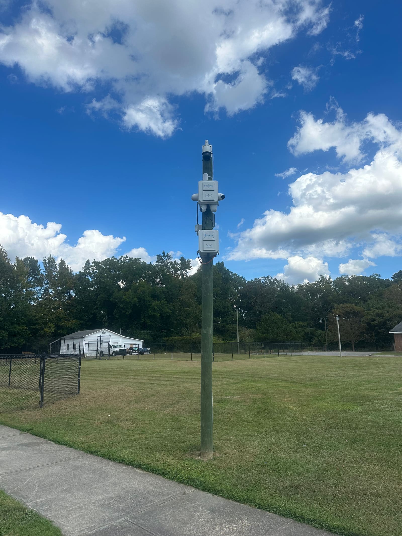 Pole-mounted surveillance camera overlooking fenced public grounds